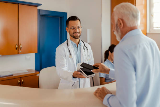 istock Old Patient Paying With Smartphone at Hospital Reception 1661421651