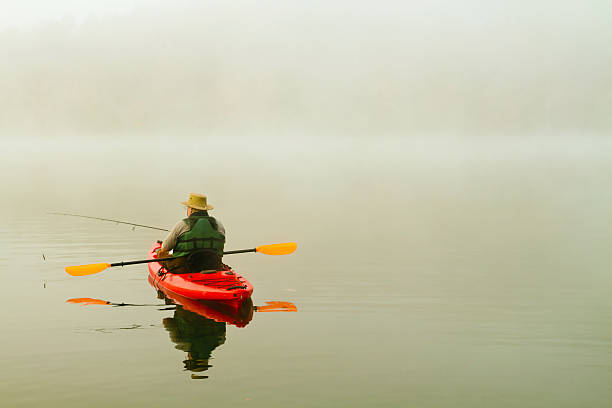 istock fisherman in red kayak, morning fog, reflection 166143049