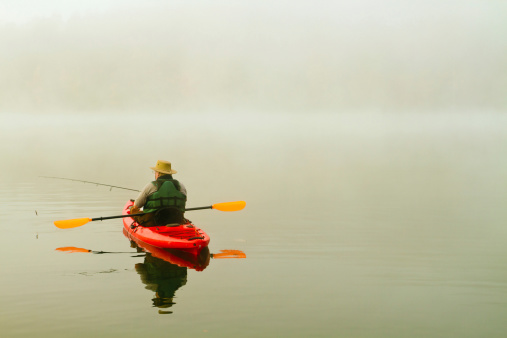 fisherman in red kayak; misty morning on Missouri lake