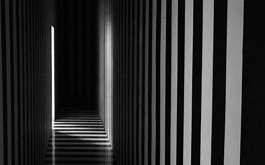 a mysterious black and white striped space in a beam of light from the door. the play of shadows and light in the corridor interior. linear perspective