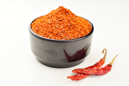 Saffron, an aromatic herb spice seasoning often used in Spanish, southern European and Middle Eastern cuisine. The dried food plant strands are piled and heaped in a white ceramic bowl. Isolated on white.