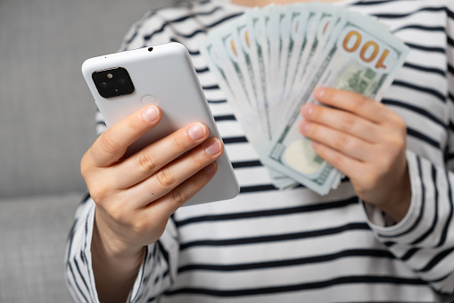 Hundred-dollar bills and a smartphone in the hands of a person