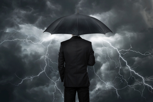 Businessman with umbrella standing in front of stormy clouds