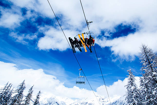 ski lift against blue sky French Alps, Haute Savoie - chair lift with three unrecognizable people against blue sky with clouds with mountains and snowy woods on the background ski resort stock pictures, royalty-free photos & images