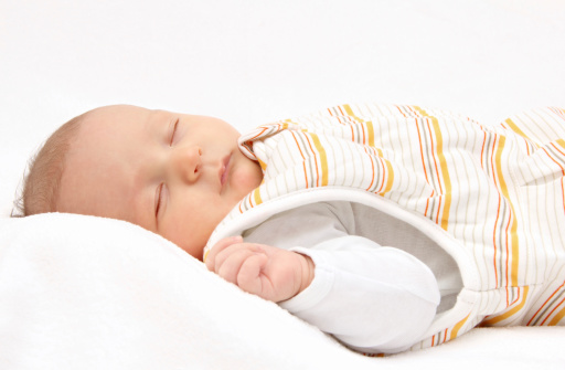 Sleeping baby on back in sleeping bag on white bed