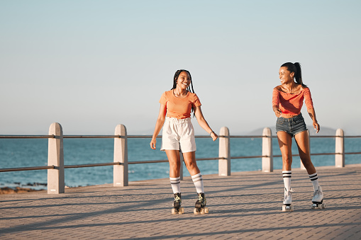 Friends roller skating on the promenade at the beach during a summer vacation in south africa. Happy, active and young girls doing a fun activity in nature on the ocean boardwalk while on holiday.
