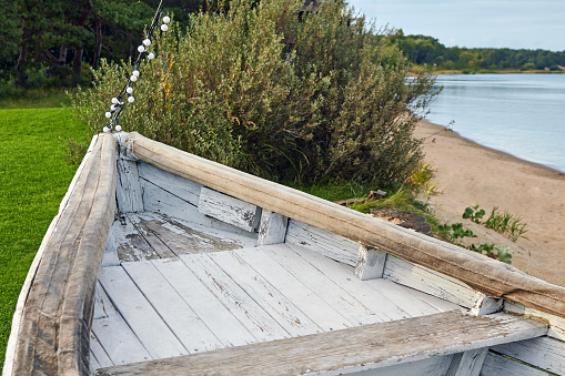 The nose of a wooden old boat painted with white paint on a green meadow on the lake.