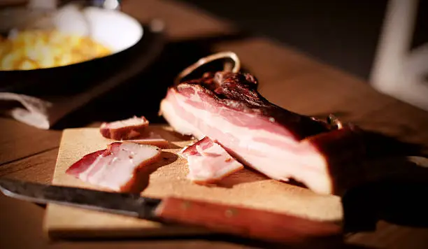 Photo of Bacon rustic cured meat on a wooden board with knife
