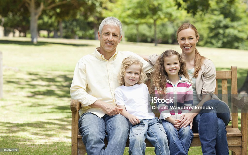 Two parents holding their children while sitting on park bench Two parents holding their son and daughter while sitting on a bench in a park Beauty Stock Photo