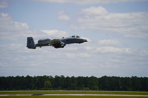 An exhilarating photograph capturing an A-10 Warthog flying at low altitude over a runway. The image showcases the aircraft's agility and power, designed for close air support missions.