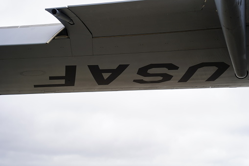 A unique perspective from beneath a C-17 Globemaster III, focusing on the 'USAF' lettering and featuring a downward-angled aileron. The photograph captures the intricate details of the aircraft's engineering while highlighting its affiliation with the United States Air Force.