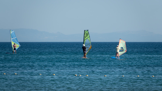 Gokceada, Canakkale Turkey July 29, 2023; Wind surfers enjoying the Aegean sea and the wind  in Gokceada Kefalos bay against the clear sky. Imbros Island.