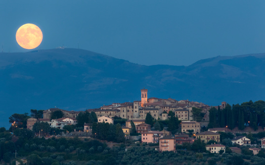 Medieval hilltop town of MonteCastello di Vibio at sunset, as an orange full moon rises over the hills beyond the Tiber valley, Umbria, Italy