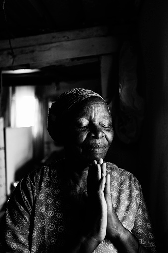 An African woman praying in her home.