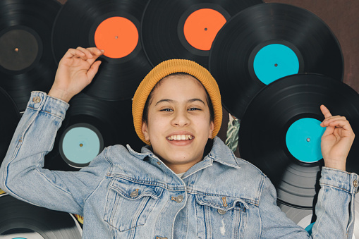 Smiling girl in yellow cap and denim jacket lying on vinyl record collection