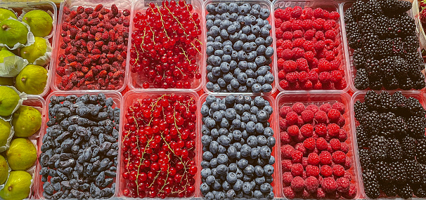 Various berries in boxes at farmer's market. Raspberry, blueberry, figs, honeysuckle, wild strawberry, currant, blackberry.