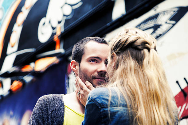 Hip young couple hugging with woman kissing his cheek on a sunny day in the city