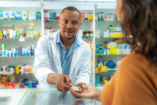 farmacia llena de medicamentos, píldoras, productos de suplementos. farmacéutico afroamericano adulto medio macho dando paquete de medicamentos a su paciente. farmacéutico negro profesional que recomienda un producto para el cuidado de la salud a un ciu - pharmacy pharmacist customer latin american and hispanic ethnicity fotografías e imágenes de stock