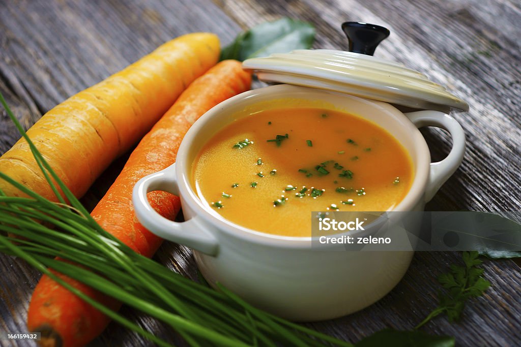 Carrot soup in a white bowl with lid and carrots on the side Carrot soup on wooden background Carrot Soup Stock Photo