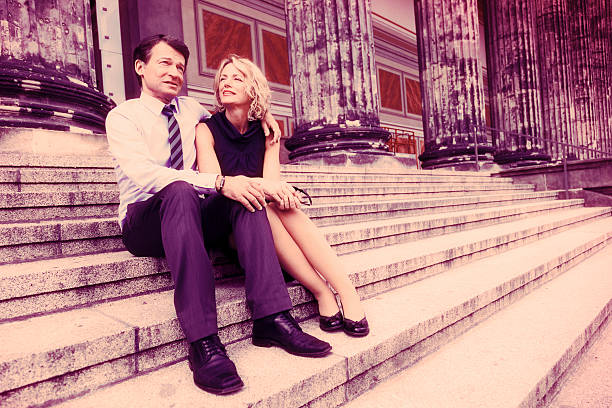 Two professionals engage in a conversation outside office buildings, with the man likely sharing industry insights with the woman, both dressed in business attire.