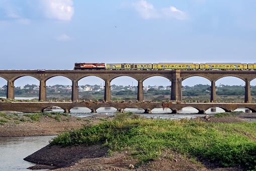 On its inaugural run, super-fast Duronto express train crossing an old stone arc bridge in Daund, Maharashtra, India.