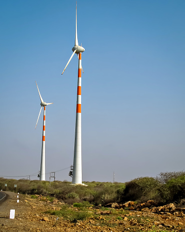 Tall Windmills distributed in an open field with nice, clear blue sky background.