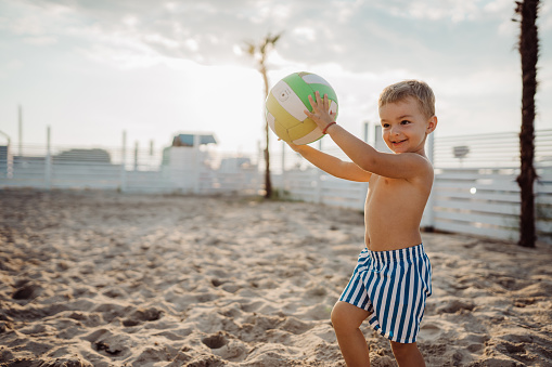 baby boy is playing with a ball at the beach