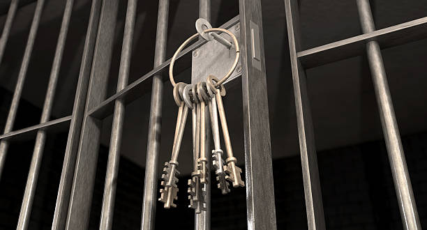 Ring of keys hanging from a slightly ajar jail cell door A closeup of the lock of a  jail cell with iron bars and a bunch of key in the locking mechanism with the door open releasing stock pictures, royalty-free photos & images