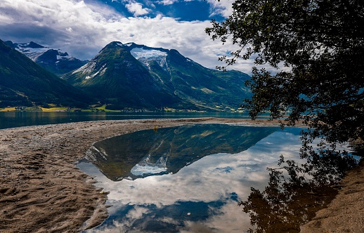 A majestic mountain peaks reflected in a tranquil lake surrounded by sandy shoreline