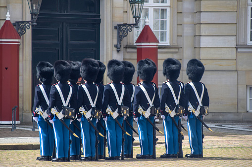 One armed soldier guard using bearskin standing in the front yard at Buckingham Palace, London, England. This picture was taken from outside the palace during the changing of The Queen's Guard, the infantry soldiers charged with guarding the official royal residences in the United Kingdom. A bearskin is a tall fur cap, usually worn as part of a ceremonial military uniform.