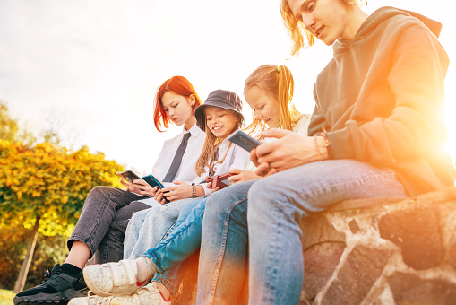 Teenager boy and a sister girls kids sitting and browsing their smartphone devices. Careless young teenhood time and a modern technology concept image.