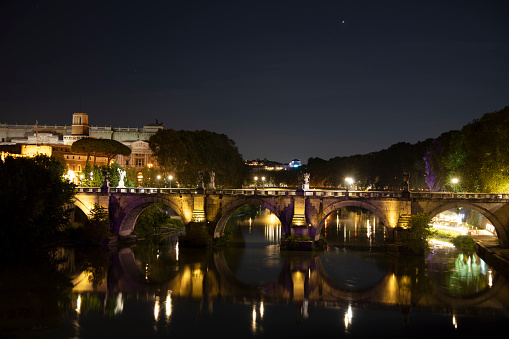 A night view of the Ponte Vittorio Emanuele II bridge in Rome, Italy, illuminated with the city lights