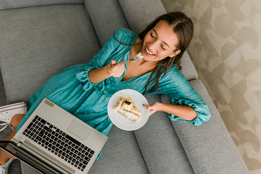 Young woman eating cake and working at home