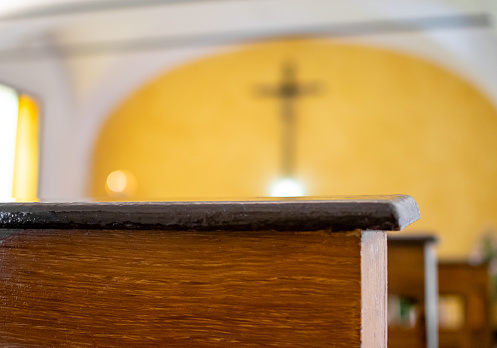 Image of Dark brown church pews with light yellow background of altar and crucifix