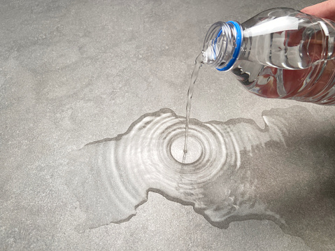 Water concept. A hand pouring water from a plastic bottle onto the granite tiled floor