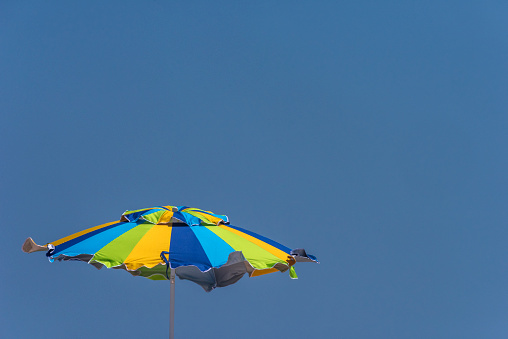 Closeup of a green, blue and yellow colored beach umbrella unfurled against a blue sky with space for copy at the top and on the right of the image.