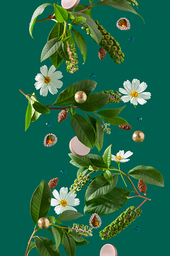 Creative levitating composition of white cosmos flowers, decorative pokeweed branches, golden spheres, glamorous baroque citrine pendants, turquoise beads, conifer cones, silver-brown cylinder prisms over dark green background.