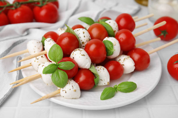 istock Caprese skewers with tomatoes, mozzarella balls, basil and spices on white table, closeup 1661896893