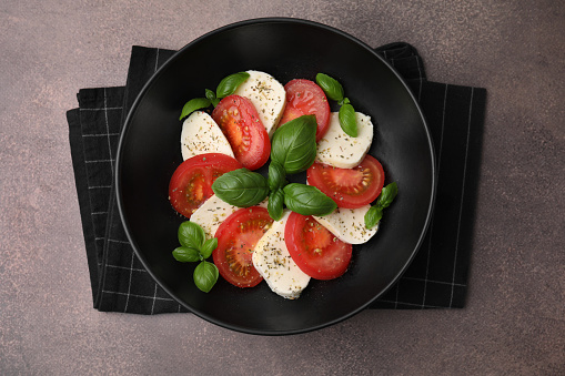 Caprese salad with tomatoes, mozzarella, basil and spices on brown table, top view