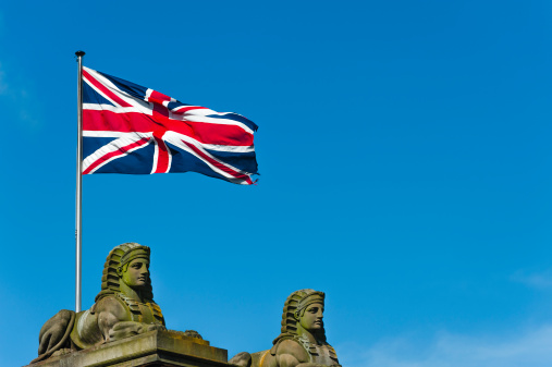 The Union Jack (UK flag) flying above two sphinxes on a bright, windy day.