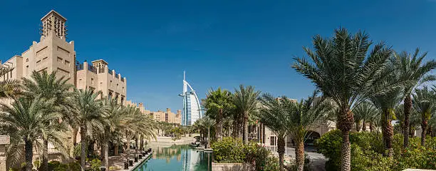 The iconic futuristic sails of the luxury Burj Al Arab hotel rising beside the traditional wind towers and tranquil palm fringed oasis of the Madinat Jumeirah on the coast of Dubai, United Arab Emirates. ProPhoto RGB profile for maximum color fidelity and gamut.