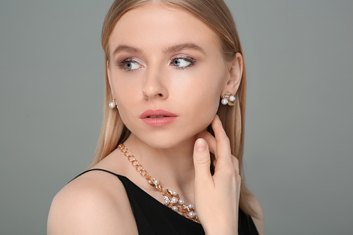 Beautiful young woman with elegant jewelry on gray background