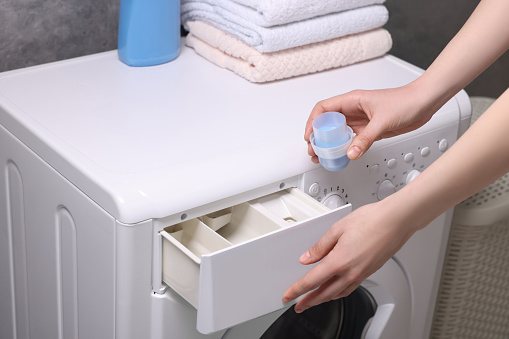 Woman pouring fabric softener from cap into washing machine, closeup