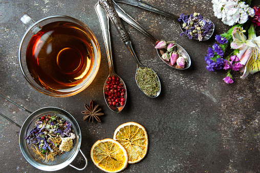 Directly above view of a tea cup. Surrounded by a variety of herbal teas and spices like Purple tea, Rose tea , Dried orange slices, Anise tea,  Melissa tea, Rosemary tea,  red peppercorns and Rosemary.