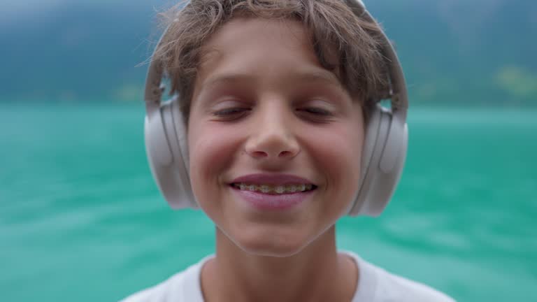 Handsome young boy putting headphones on over the ear smiling at camera, portrait face close-up of teenager kid listening to audio