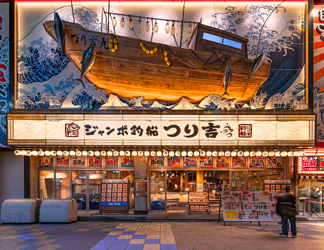 osaka, japan - dec 04 2022: Fish and seafood restaurant Jumbo Tsuribune Tsurikichi with a fishing boat sailing in sea waves evocating The Great Wave of the Ukiyo-e master Katsushika Hokusai on facade.