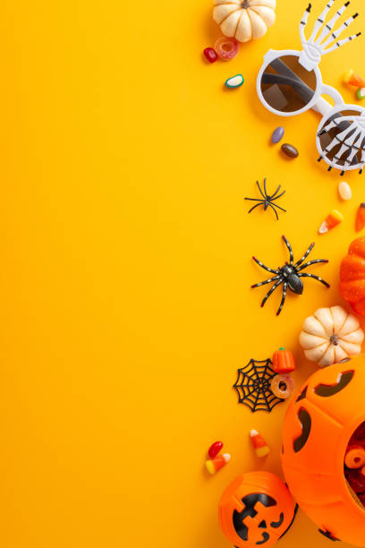 istock Join in kids' trick or treating joy. Overhead vertical view snapshot displaying pumpkin basket with candies and Halloween decorations on orange isolated backdrop, great for text or advert integration 1662002435