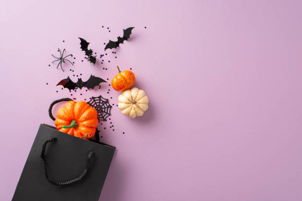 istock Spreading Halloween happiness through thoughtful gifting gestures. Seen from above, a black paper gift bag meets Halloween decorations on a purple isolated backdrop, providing space for ads or text 1662003036