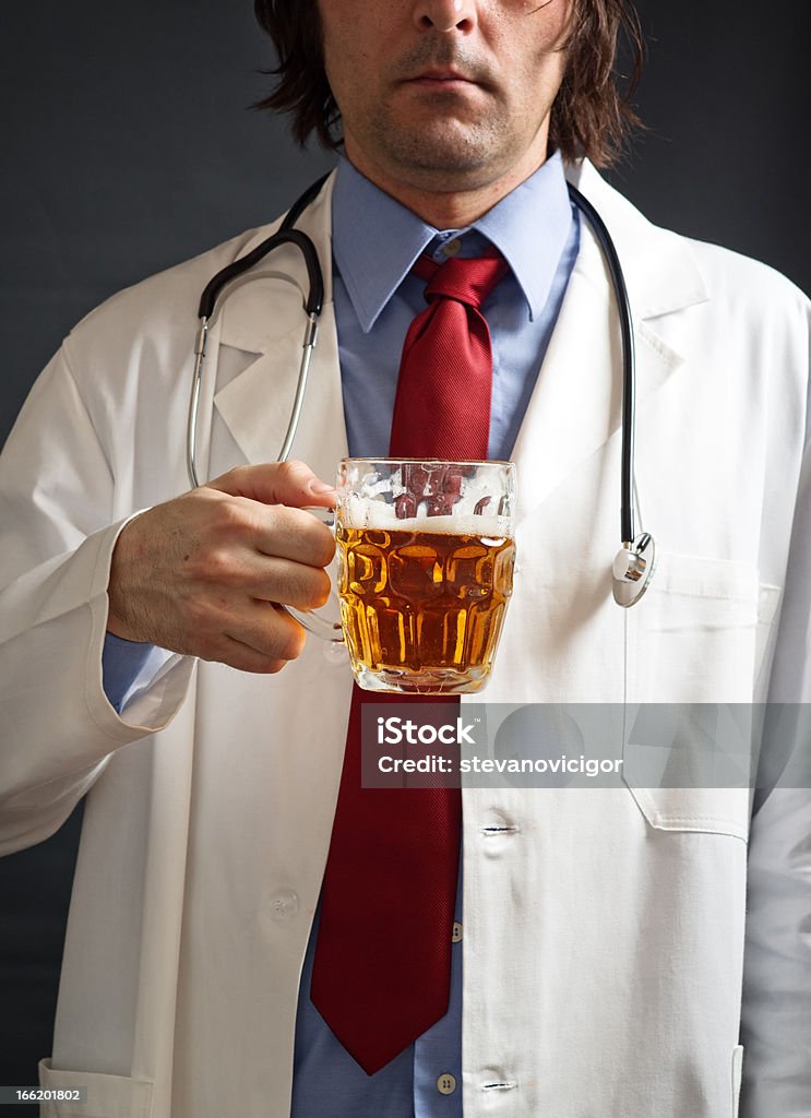 Doctor is drinking beer Male doctor is drinking light beer from the glass jug. One glass of beer a day concept. Beer - Alcohol Stock Photo