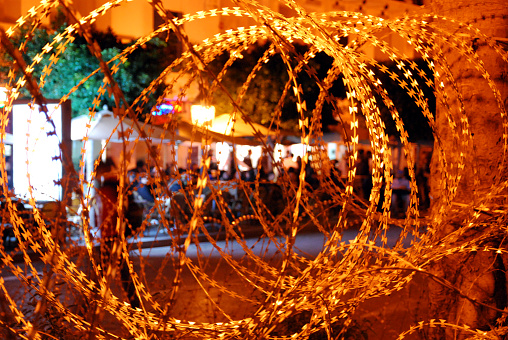 In December 2011, amid a golden evening in Tunis, Tunisia, closely-detailed rolls of razor wire glisten, symbolizing security measures. Silhouetted café patrons bear silent witness to Tunisia's historic transformation.